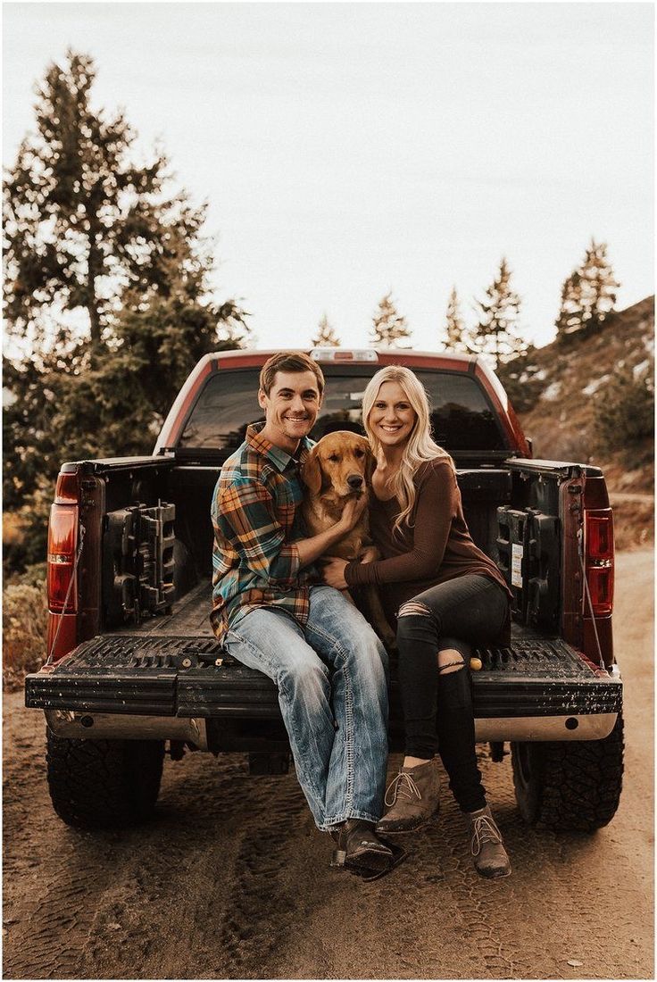 a man and woman sitting in the back of a truck with a dog