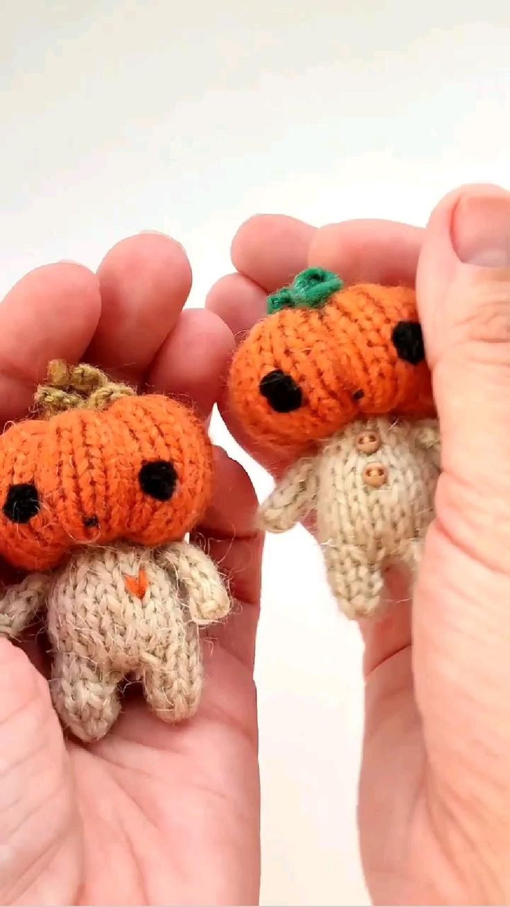 two hands holding small knitted pumpkins with faces on them, one being held by the other