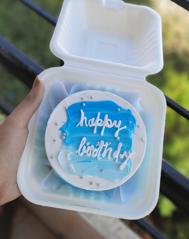 someone holding up a birthday cake in a plastic container with the words happy birthday written on it