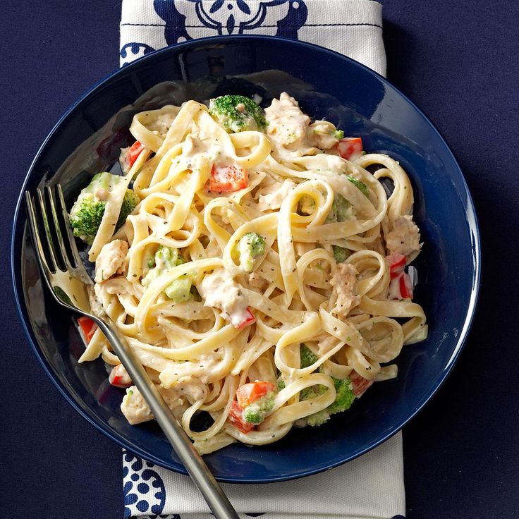 a blue plate topped with pasta and veggies next to a silver fork on top of a white napkin