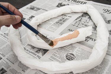 a person is using a paintbrush to decorate a paper towel wreath with newspaper pages