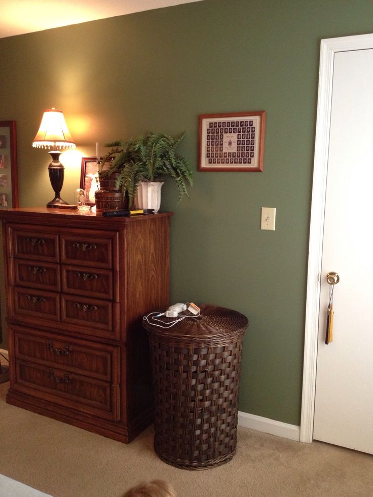 a bedroom with green walls and a brown wicker basket next to the dresser in front of it