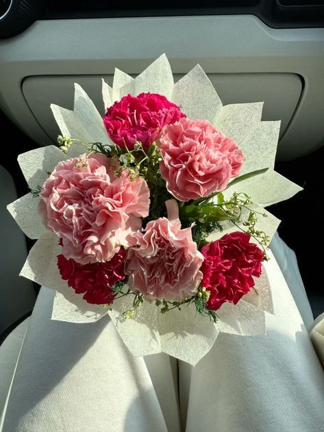 pink carnations and red carnations wrapped in white paper on the back seat of a car