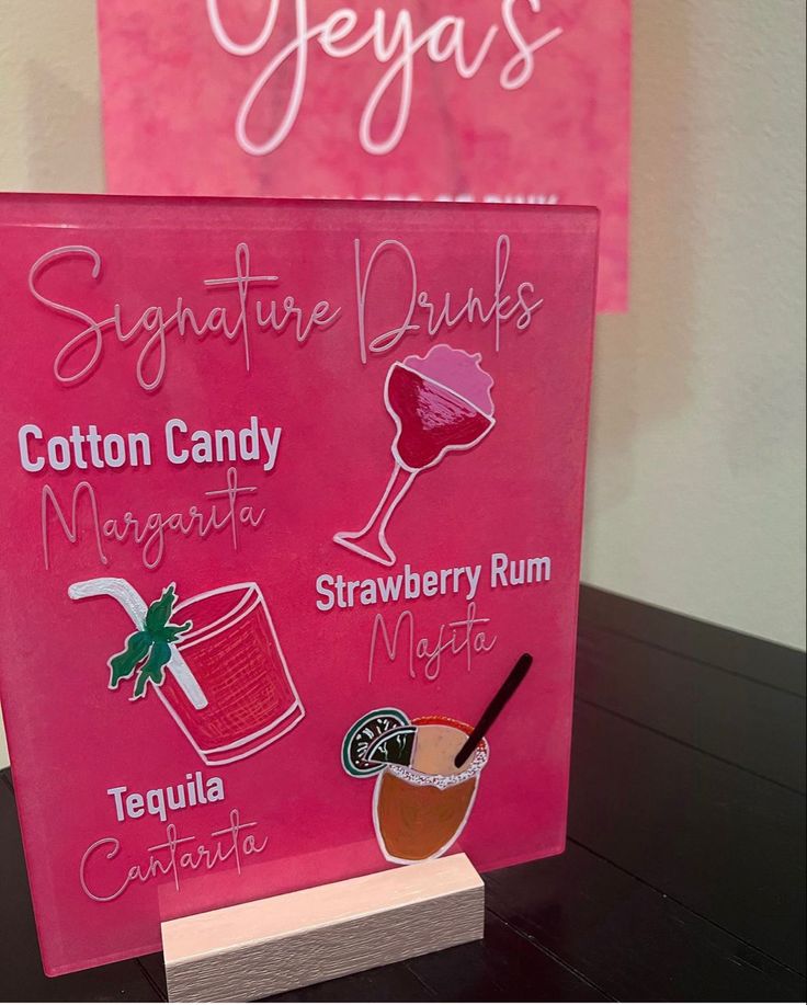 a pink sign with different types of drinks on it next to a wooden block that says signature drinks