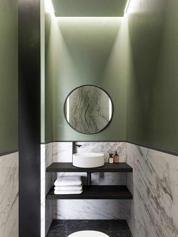 a bathroom with green walls and marble counter tops, along with a round mirror on the wall