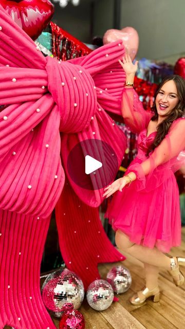 a woman in a pink dress is dancing with balloons and other decorations behind her on the floor