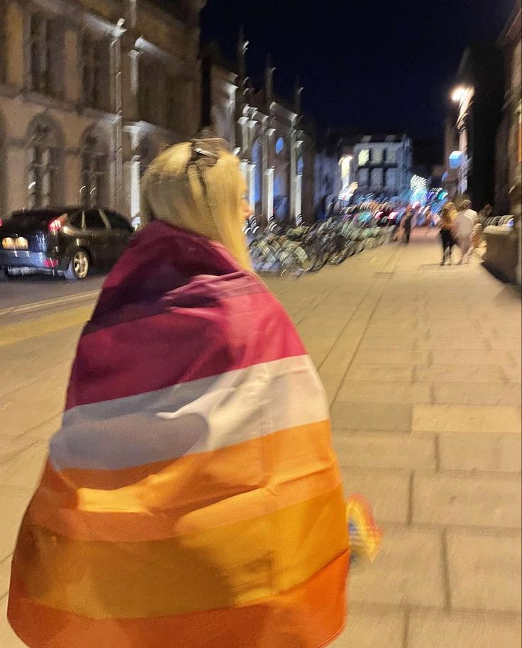 a woman walking down the street holding an orange, white and pink flag on her back