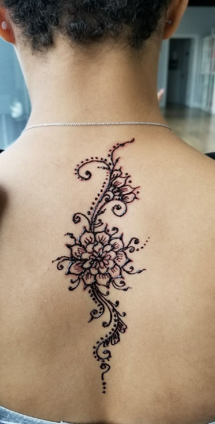 the back of a woman's neck with an intricate tattoo design on her left shoulder