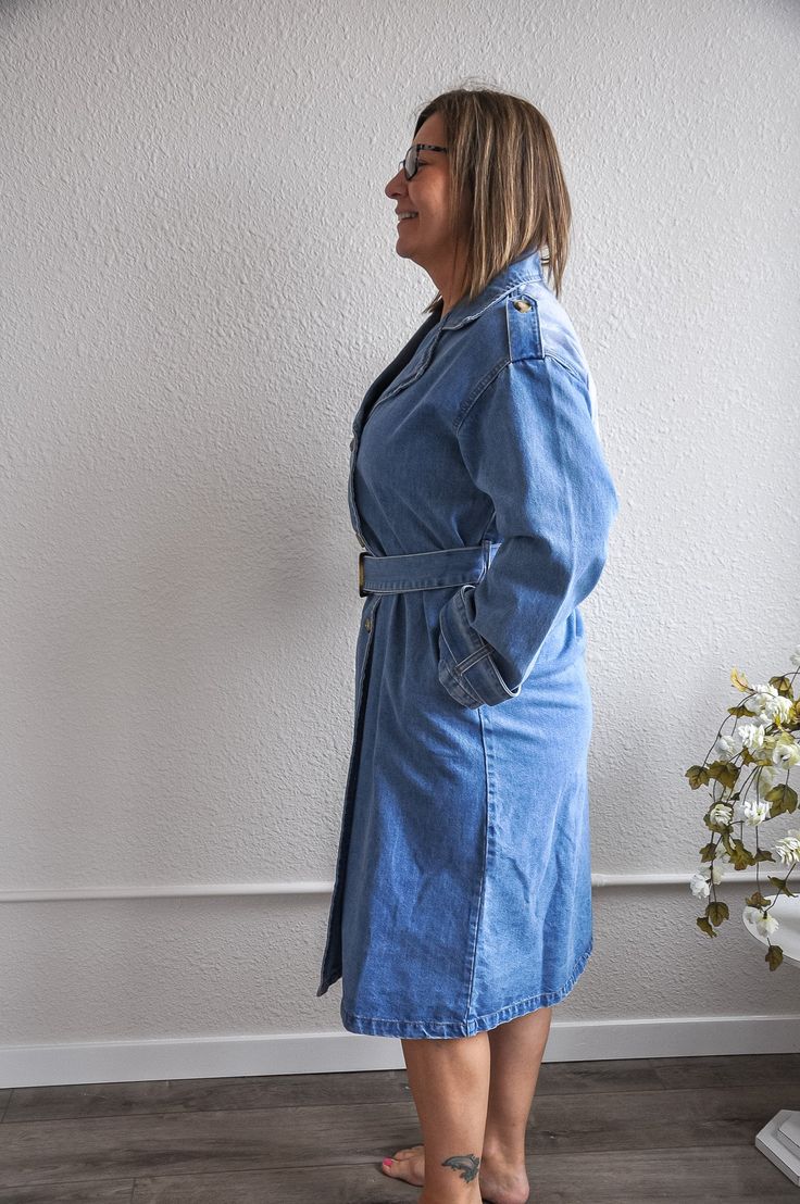 This medium denim trench coat exudes timeless elegance and casual sophistication. The medium denim wash gives it a classic yet contemporary look, while the waist belt detail adds a touch of tailored refinement, allowing for a customizable fit. With its long denim coat fit, this piece offers both warmth and style, making it a versatile addition to any wardrobe. The classic button closure and long sleeves provide a traditional trench coat silhouette, perfect for layering over various outfits. The Denim Outerwear With Belt Loops For Work, Chic Medium Wash Belted Denim Dress, Long Sleeve Denim Outerwear With Belt Loops, Long Sleeve Denim Jacket With Belt Loops, Casual Denim Outerwear With Belt Loops, Belted Denim Jacket For Workwear, Fall Workwear Medium Wash Denim Dress, Denim Blue Belted Outerwear For Spring, Spring Denim Blue Belted Outerwear