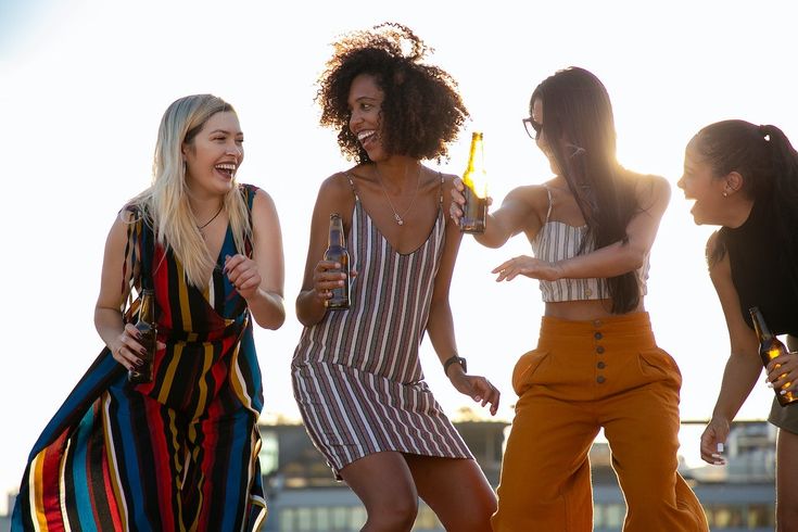 four young women are laughing and having fun on the roof top, while one woman is holding a beer in her hand