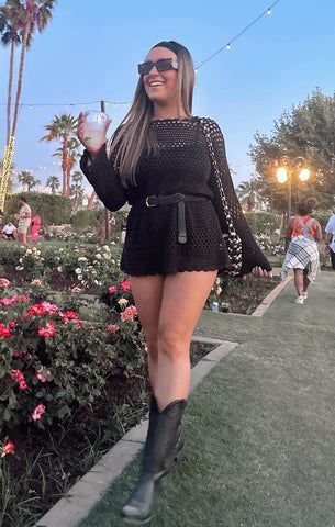 a woman in black dress and cowboy boots walking down the sidewalk with her hand on her hip