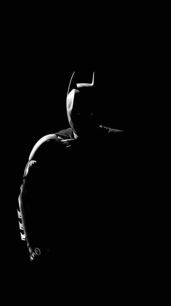 black and white photograph of batman standing in the dark with his head turned to the side