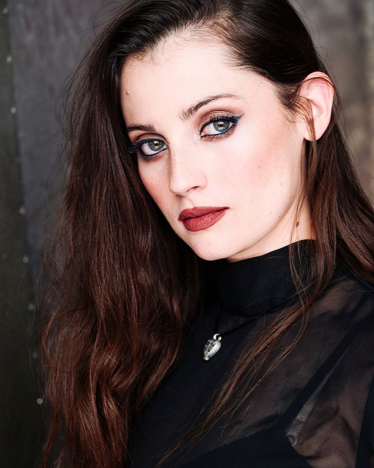 a woman with long brown hair and blue eyes wearing a black top is looking at the camera