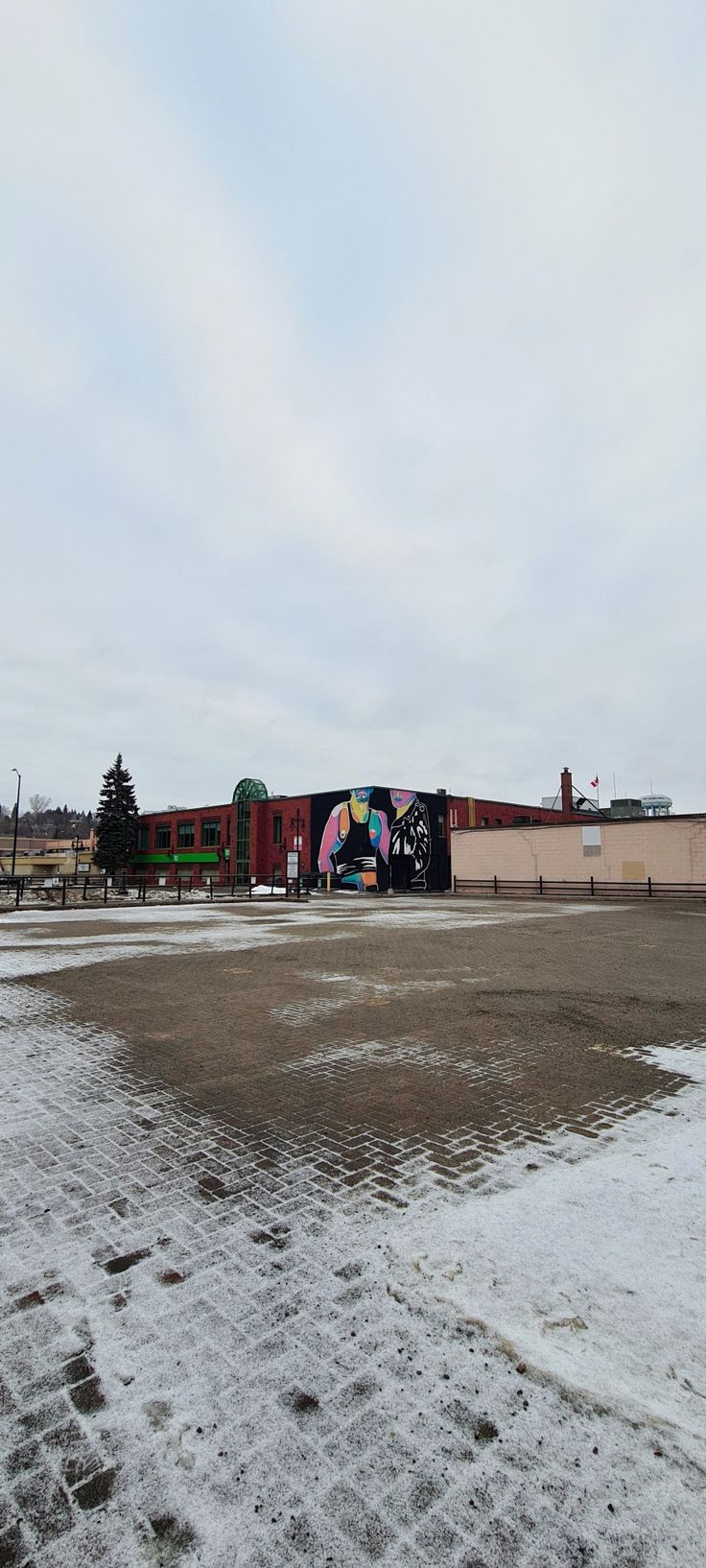 an empty parking lot in front of a building with graffiti on the side and snow on the ground