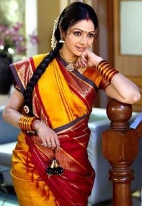 a woman in a yellow and red sari posing on a wooden railing with her hand under her chin