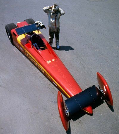 a man standing next to a red and yellow race car on top of a parking lot