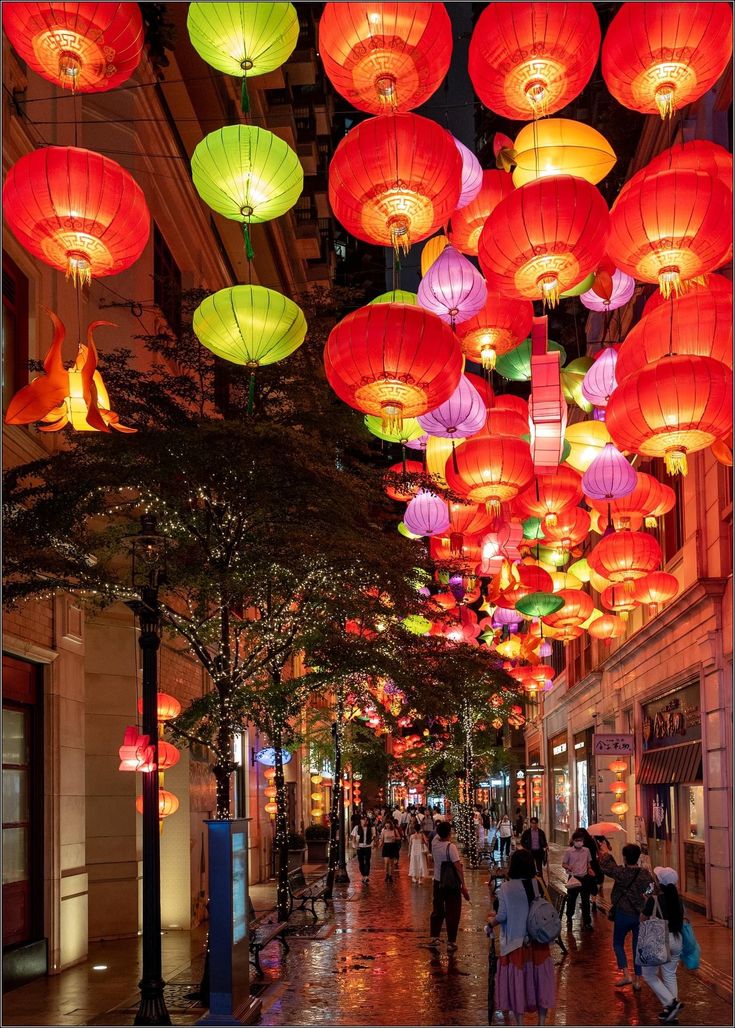 many red and yellow lanterns are hanging from the ceiling in this shopping mall, along with people walking down the street