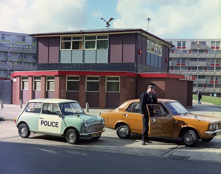 two old cars parked in front of a building with a police officer standing next to it