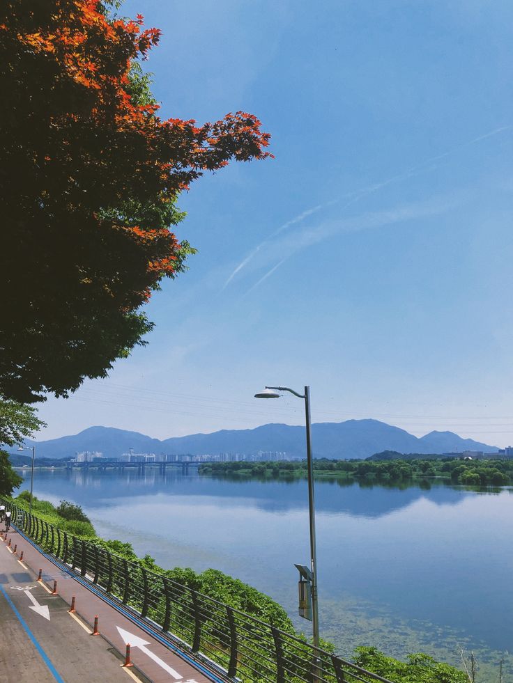 people riding bikes on the side of a road next to a body of water with mountains in the background