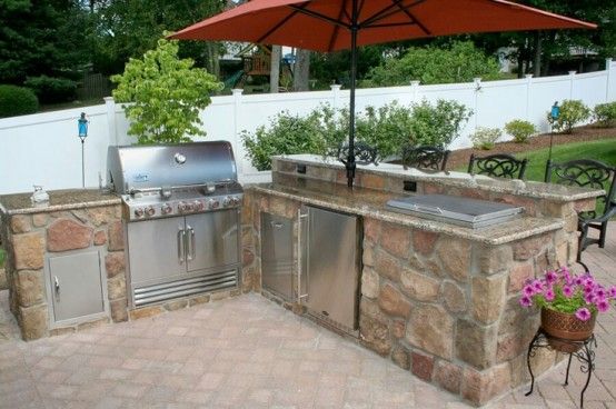 an outdoor kitchen with grill and umbrella over it