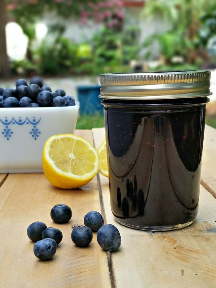 blueberries and lemons sit on a wooden table next to a jar of jam