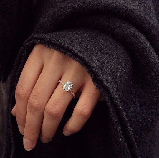 a woman's hand with a diamond ring on her left hand, wearing a black coat