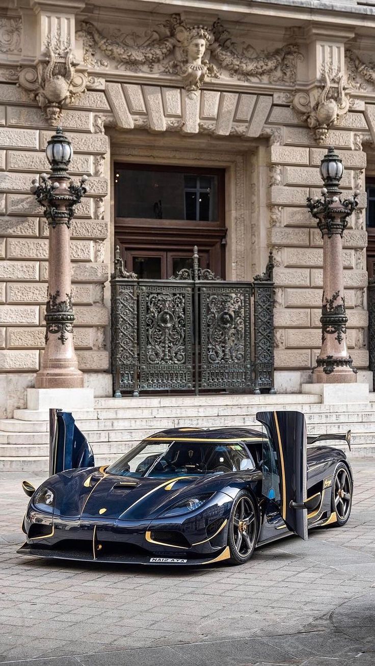 a black sports car parked in front of a building with its doors open and the door opened