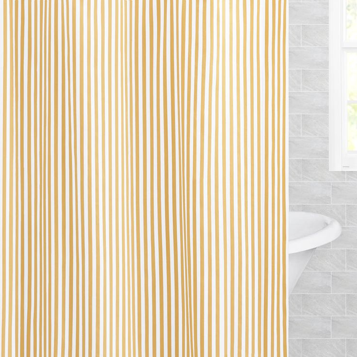 a yellow and white striped shower curtain next to a bathtub with a window in the background