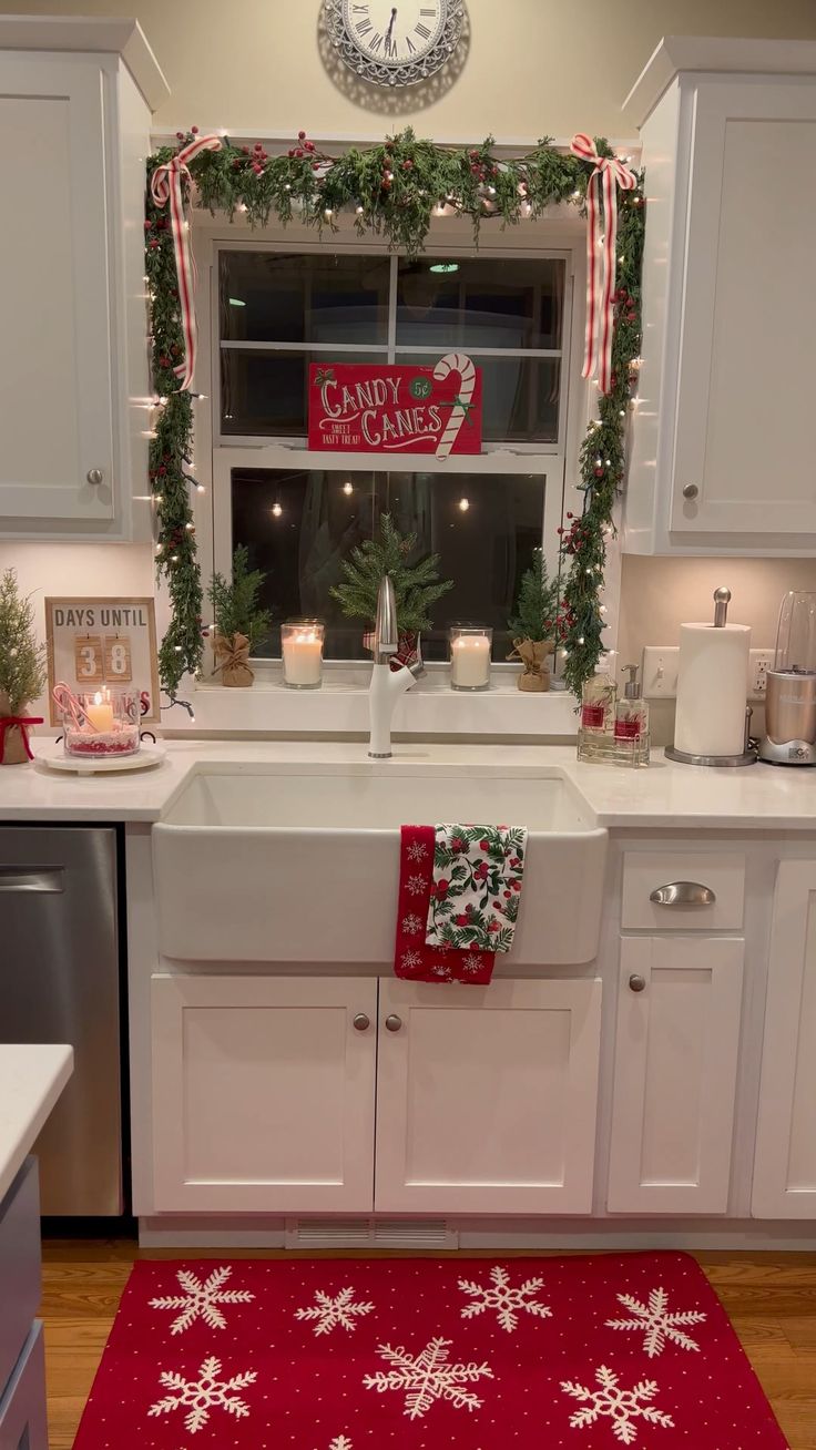 a kitchen decorated for christmas with red and white decorations on the window sill, wreaths and candles