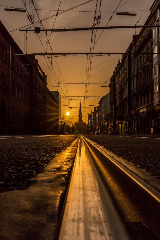 the sun is setting on an empty street with power lines above it and buildings in the background