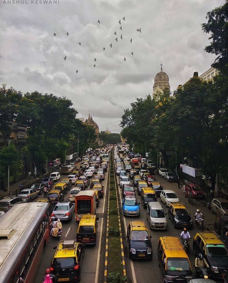 a busy street filled with lots of traffic under cloudy skies and birds in the sky