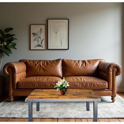 a brown leather couch sitting in a living room next to a wooden table and potted plant