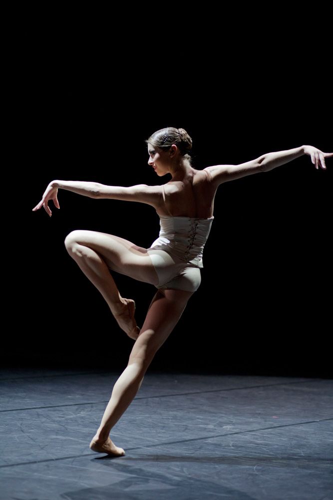 a woman in white leotard standing on one leg with her legs spread out