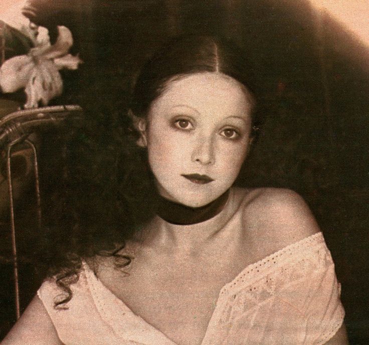 an old photo of a woman wearing a white dress and posing for the camera with flowers in her hair