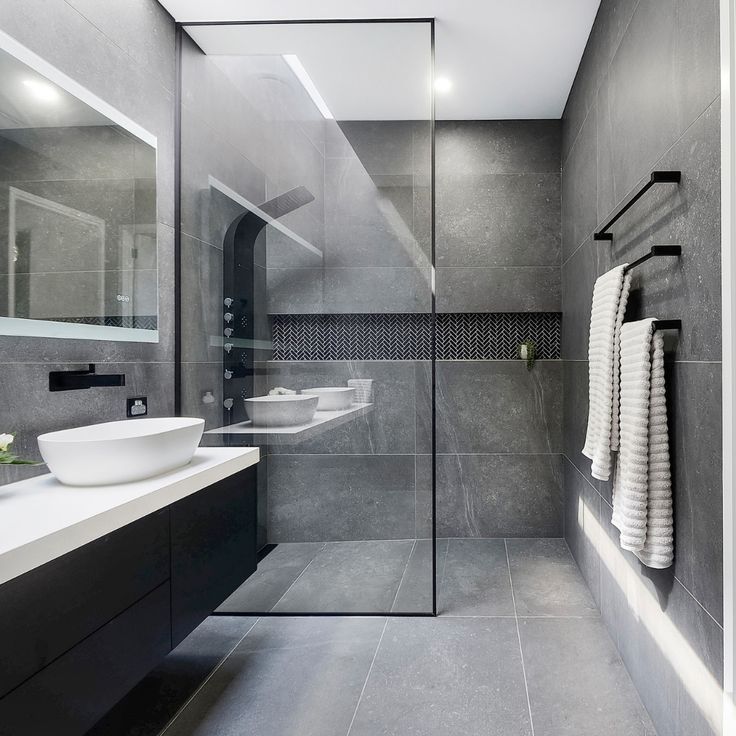 a modern bathroom with grey walls and flooring is seen in this image, there are towels hanging on the rack next to the sink