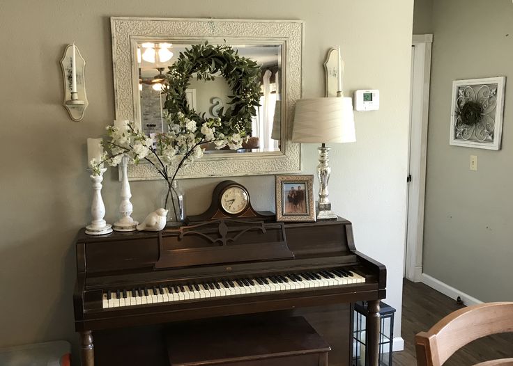 a living room with a piano, mirror and wreath on the wall in front of it