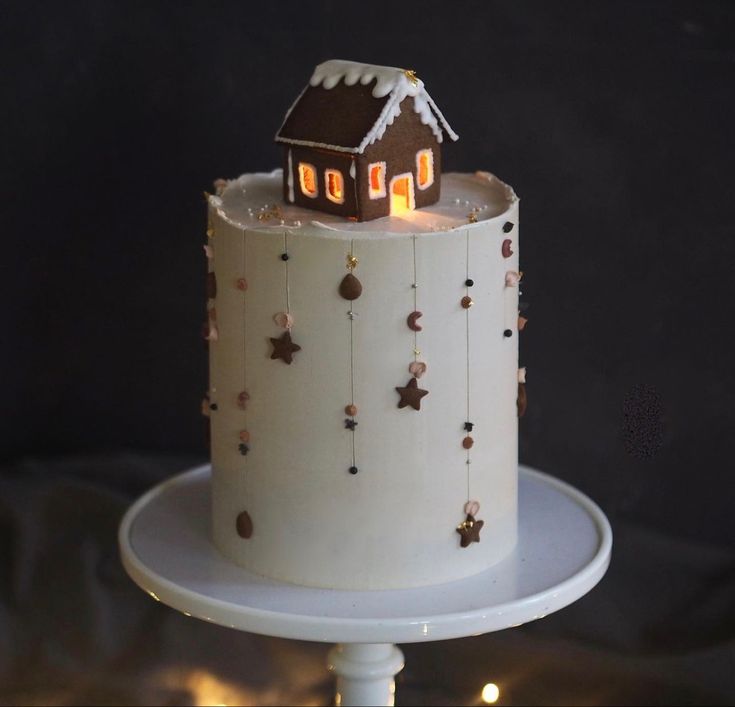 a white cake with a brown house on top and stars around the edges is sitting on a pedestal