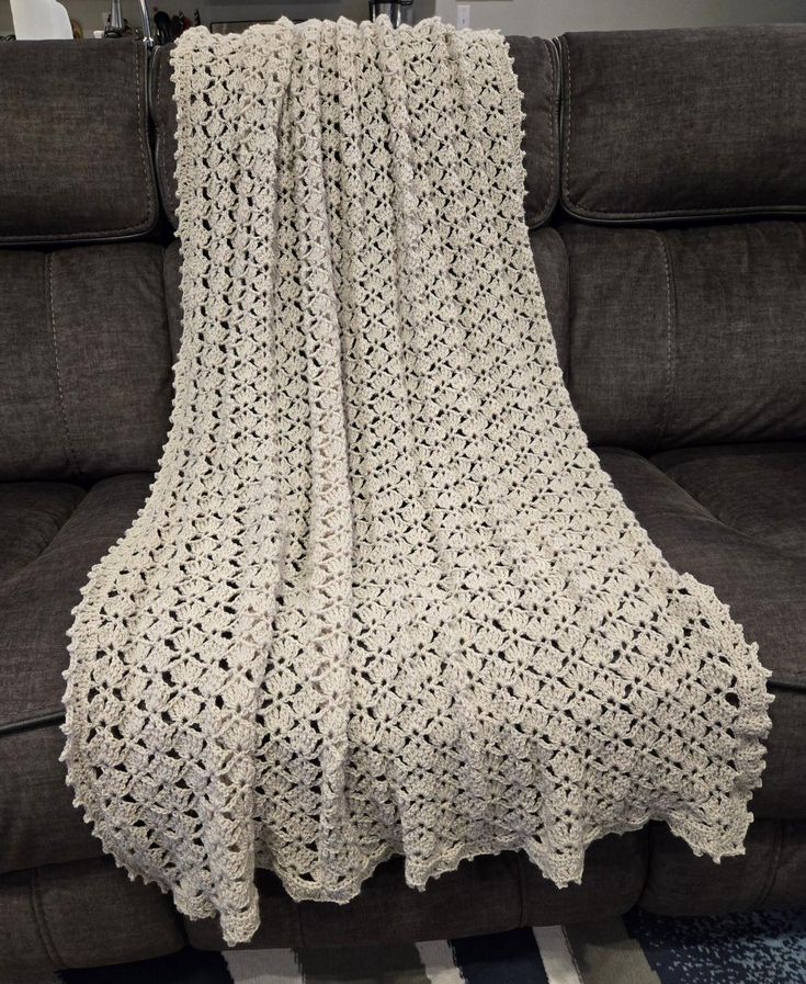 a white crocheted blanket sitting on top of a couch next to a black chair