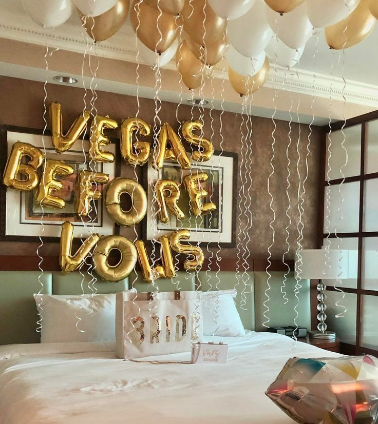 balloons are hanging from the ceiling above a bed with white sheets and gold foil decorations