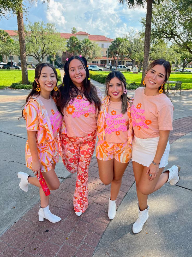 four girls in matching outfits posing for the camera on a brick sidewalk with palm trees behind them