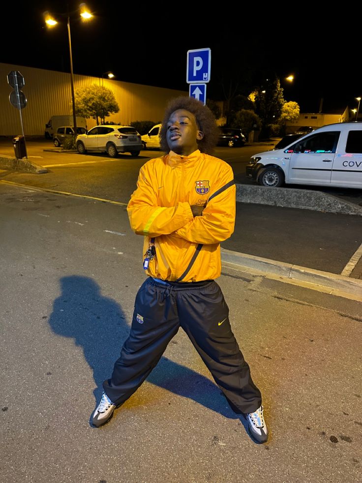 a man with his arms crossed standing in the middle of the street wearing yellow jacket and blue pants