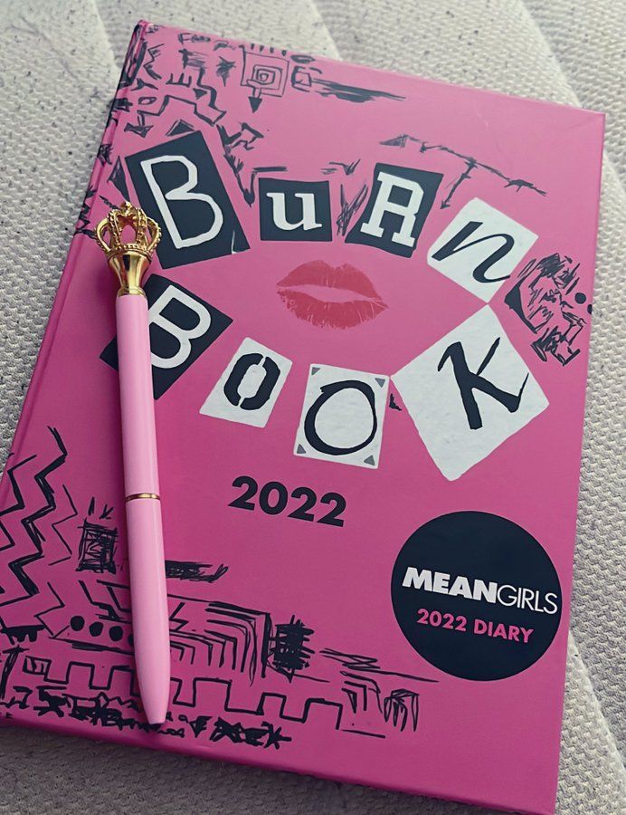 a pink notebook with the words burn book written on it and a pen resting on top