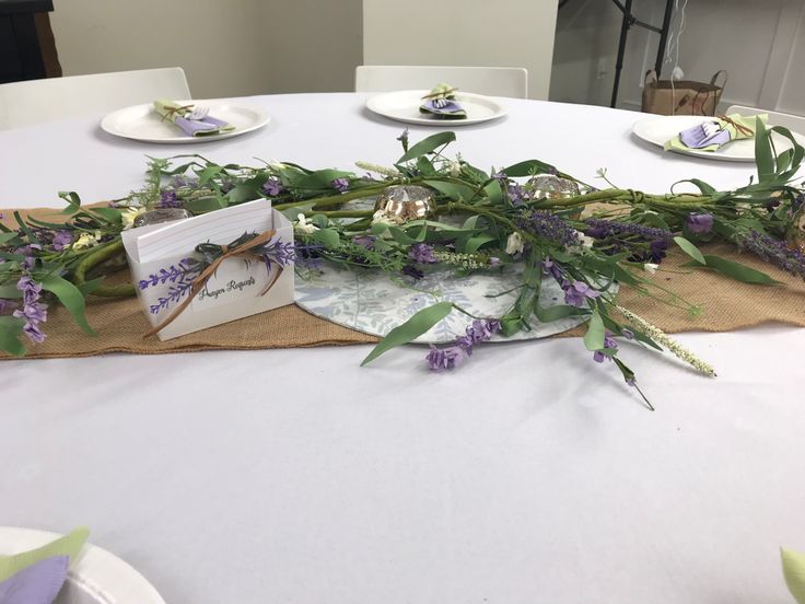 the table is set with purple flowers and greenery