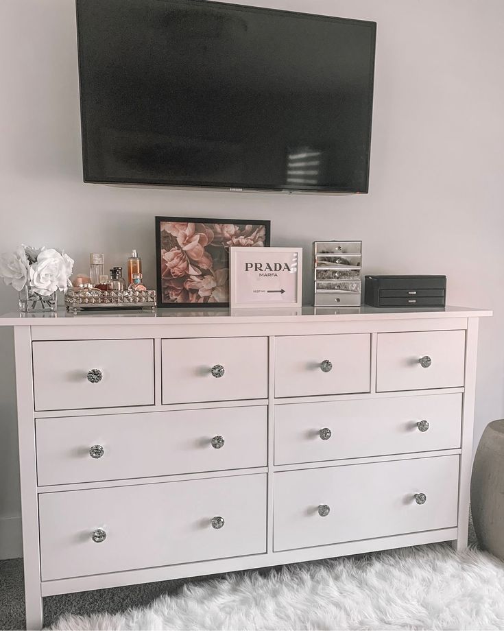 a white dresser with drawers and a flat screen tv mounted above it