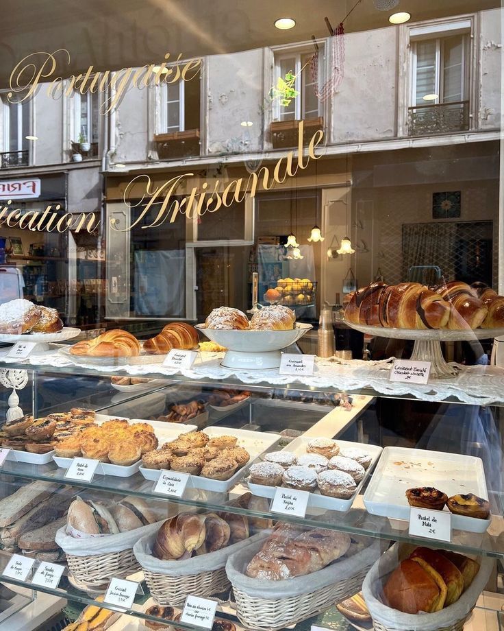 an assortment of breads and pastries on display in a bakery shop front window