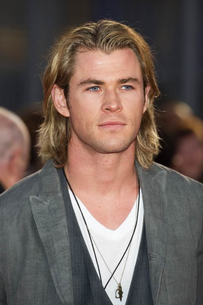 a man with long hair wearing a gray suit and white t - shirt is looking at the camera