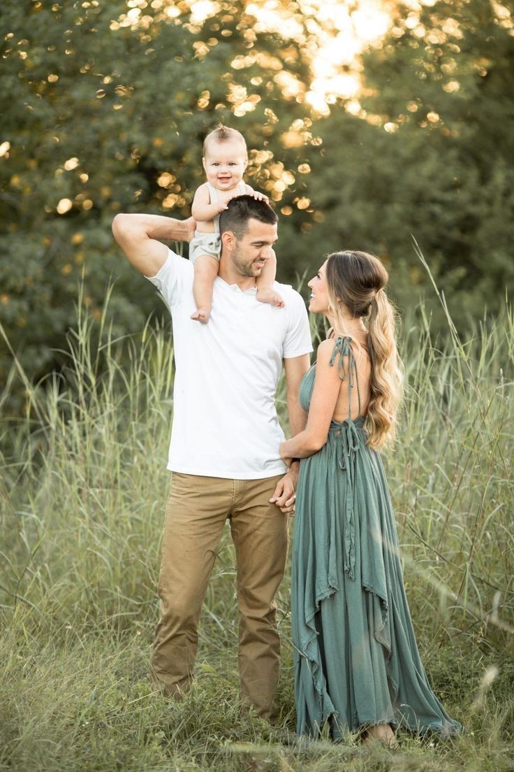 a man and woman holding a baby while standing in tall grass