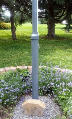 a light pole in the middle of a flower bed with purple flowers around it and trees behind it