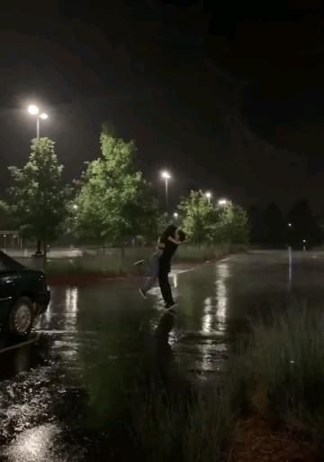 a man standing in the rain next to a parked car at night with its lights on