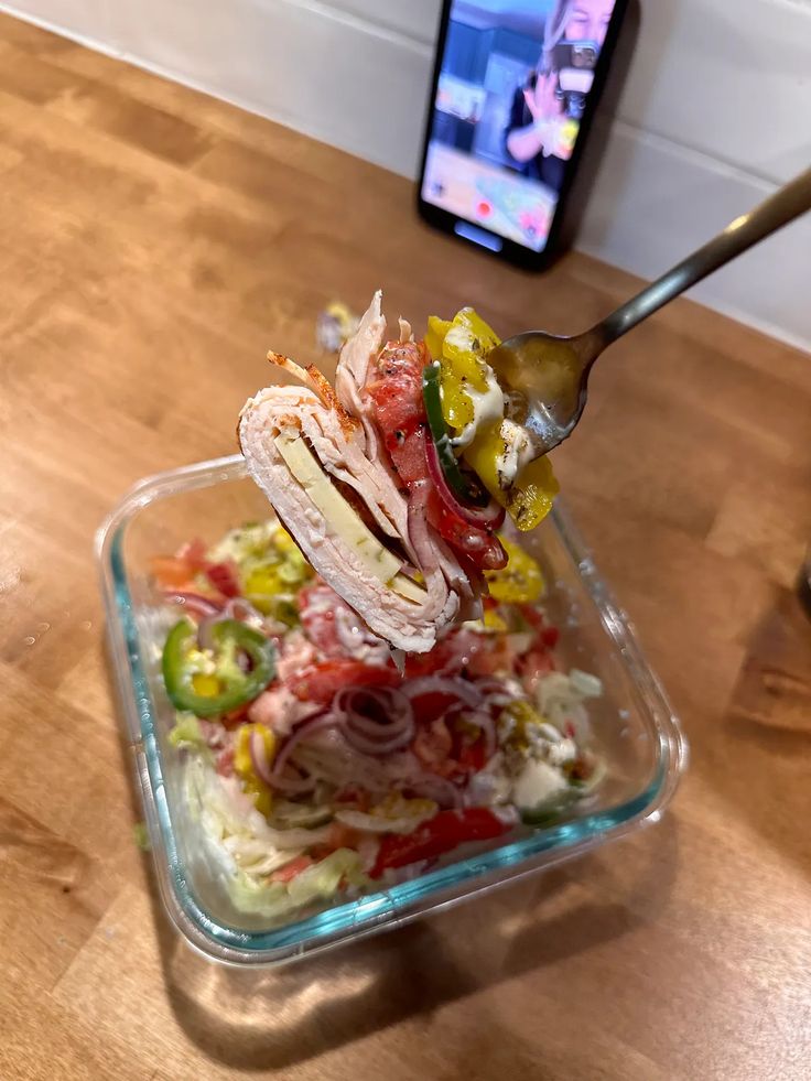 a salad in a glass dish being spooned with a plastic fork on a wooden table